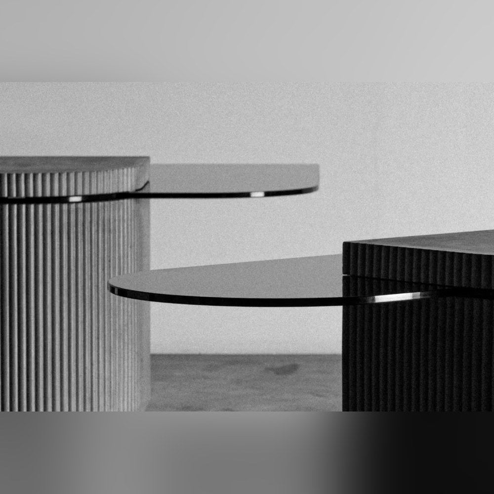 Détail en noir et blanc des plateaux en verre teinté de deux tables Strut au pied en béton cannelé