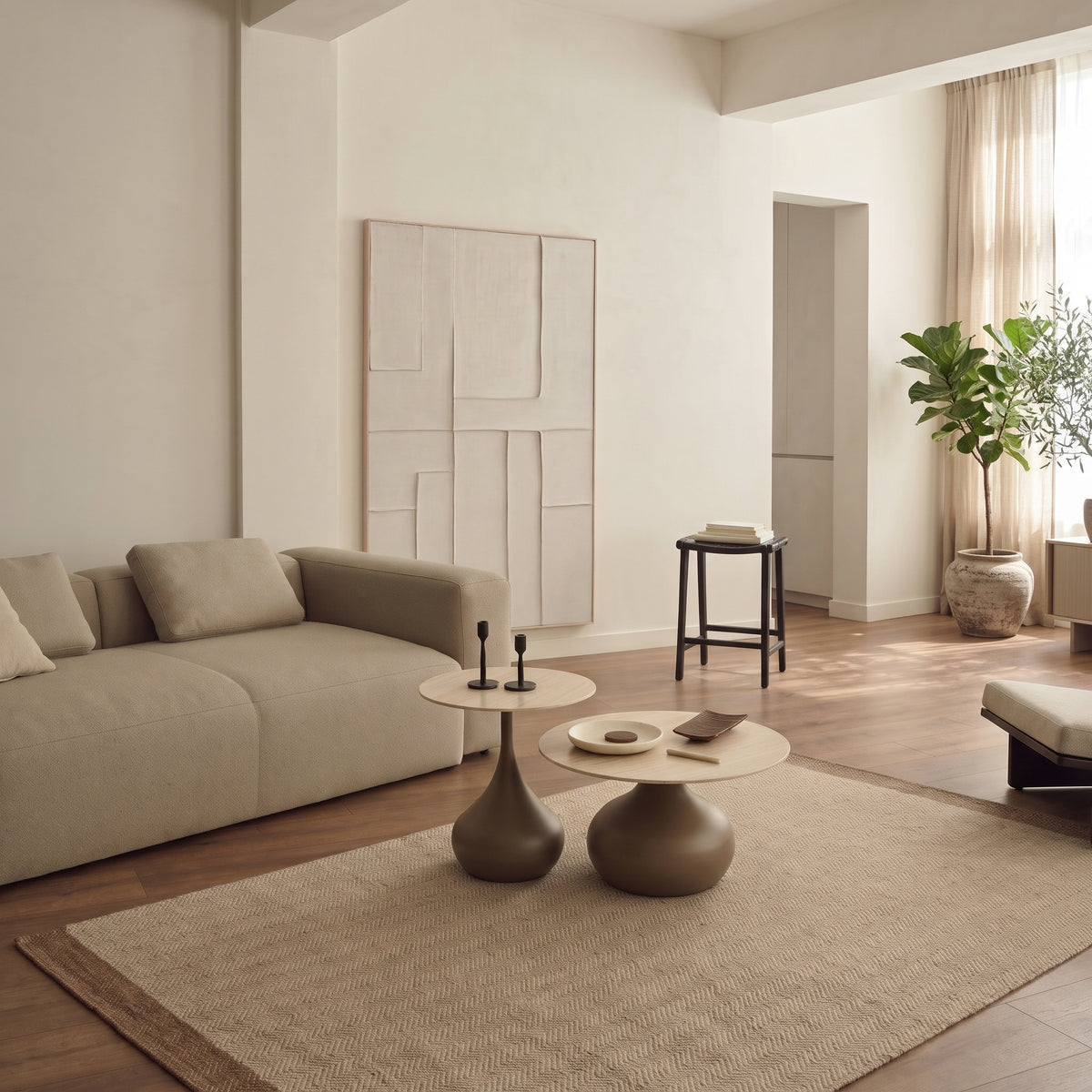 Lot de 2 tables basses Pienza dans un grand salon clair, devant un canapé beige, sous un tableau en relief