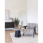 Table basse Brito à côté d'un fauteuil bouclé gris devant un miroir arche à cadre doré
