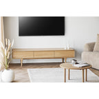 Table basse ronde Jena devant un meuble TV en chêne à côté d'un canapé bouclé