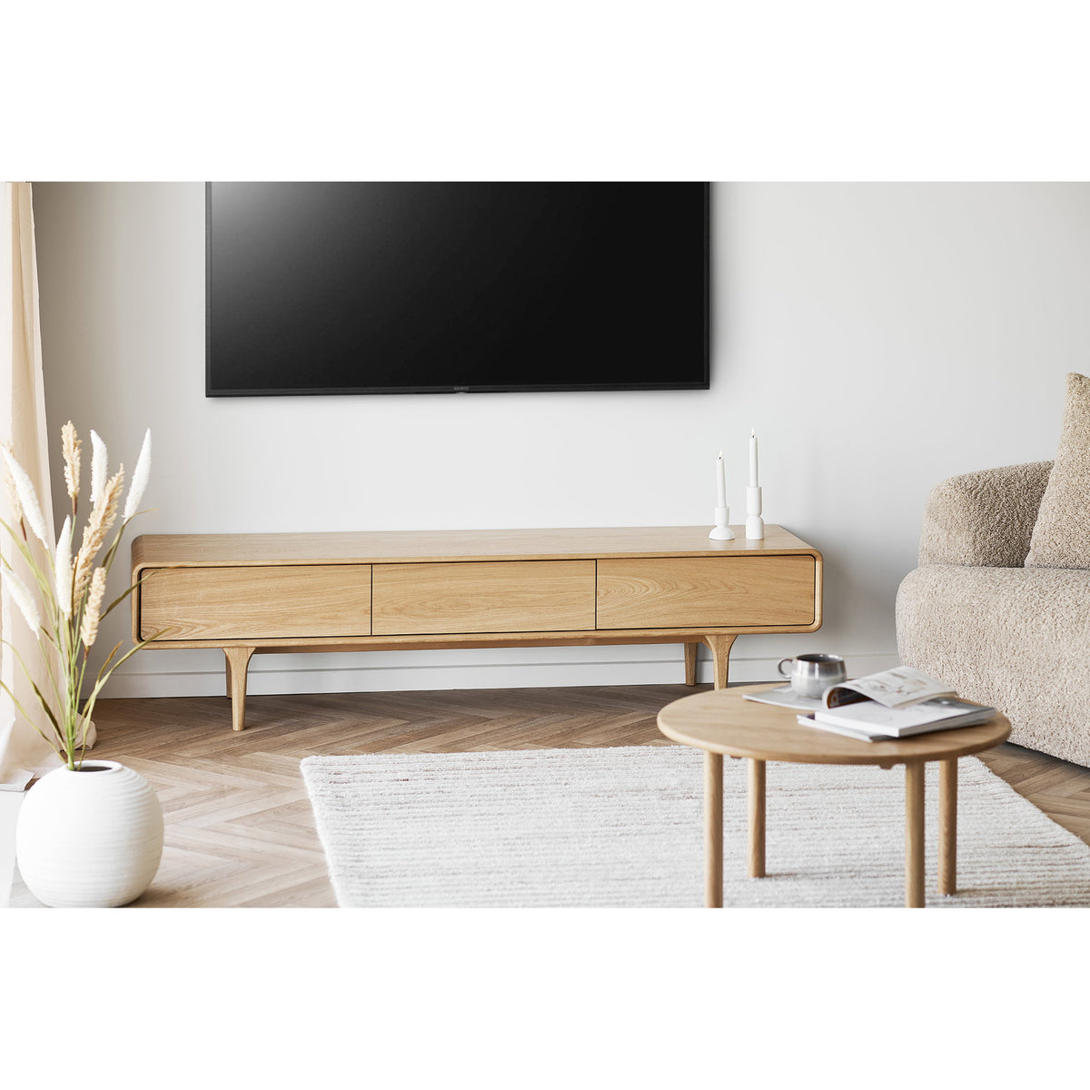 Table basse ronde Jena devant un meuble TV en chêne à côté d'un canapé bouclé
