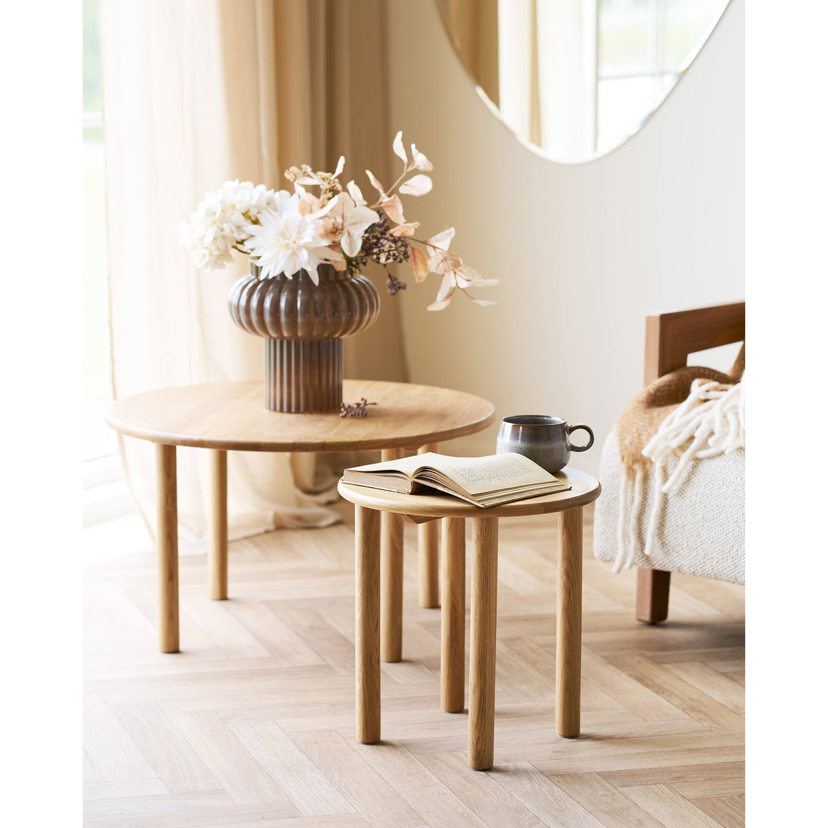 Table basse ronde Jena en chêne avec un vase côtelé et une petite table d'appoint ronde assortie près d'un fauteuil