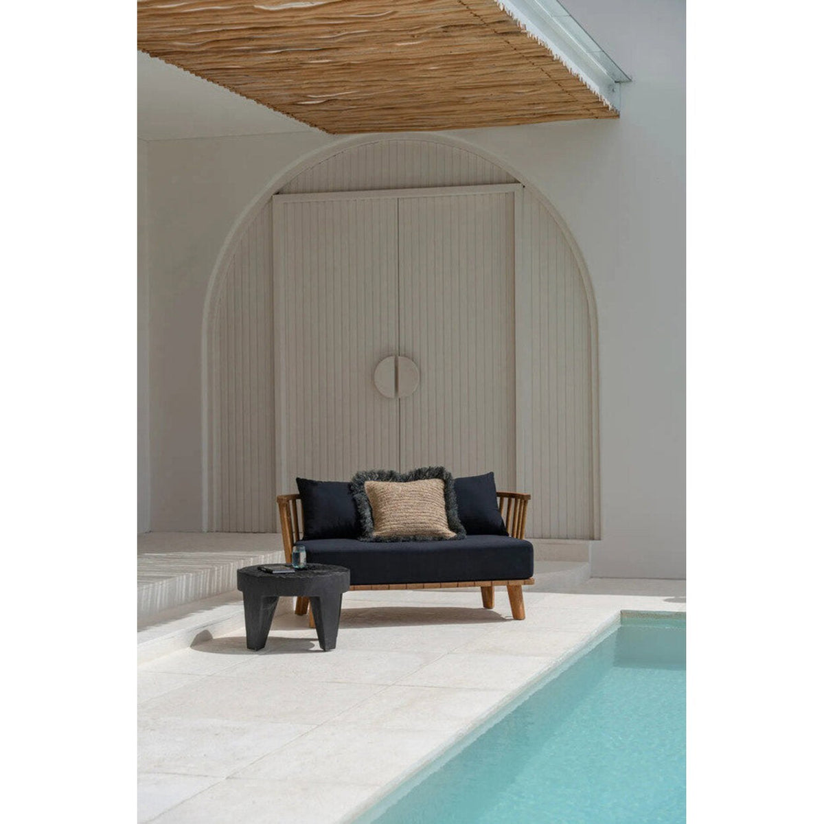 Table basse Madero en suar noir devant une banquette en bois avec des coussins sombres