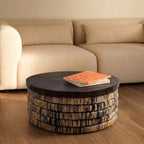 Table basse ronde Magani devant un canapé beige sur un parquet avec deux livres posés sur le plateau