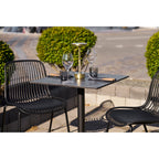Table bistrot effet marbre dressée avec des verres à vin et une lampe dorée entre deux chaises noires