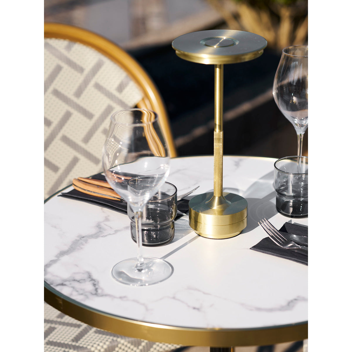 Plateau effet marbre de la table bistrot dressé avec des verres des couverts et une lampe dorée