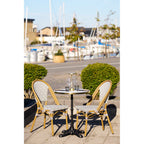 Table bistrot dressée sur une terrasse au bord d'un port avec deux chaises de bistrot