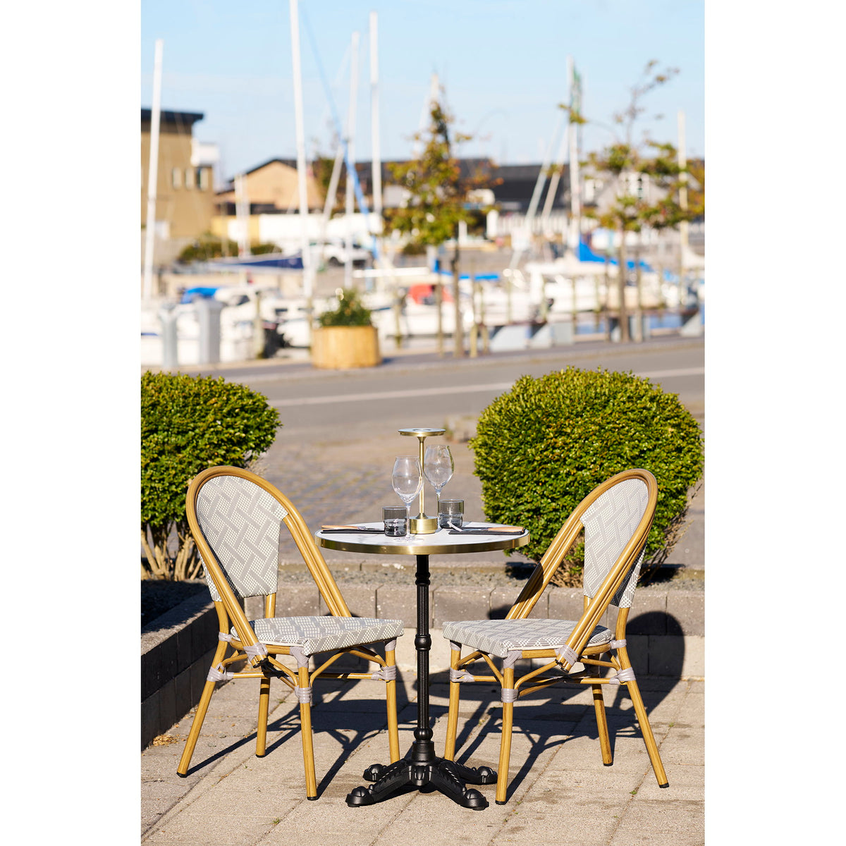 Table bistrot dressée sur une terrasse au bord d'un port avec deux chaises de bistrot