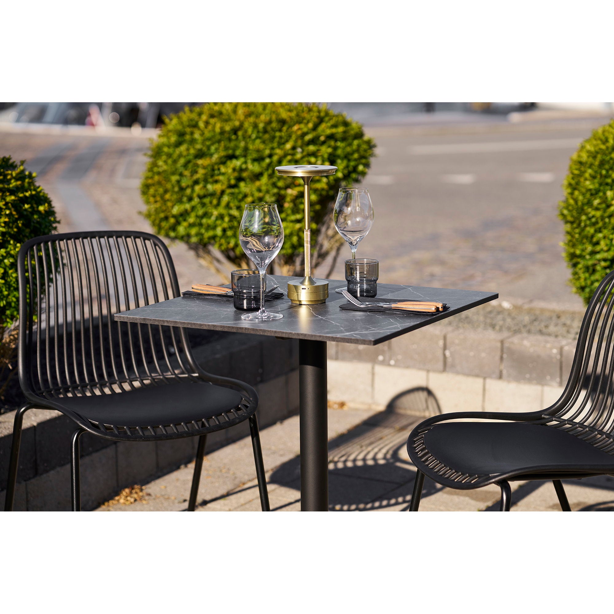 Table bistrot marbre noir aluminium dressée verres à vin lampe dorée terrasse chaises filaires noires