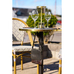 Table bistrot dressée de verres et d'une lampe dorée avec un sac suspendu à son crochet