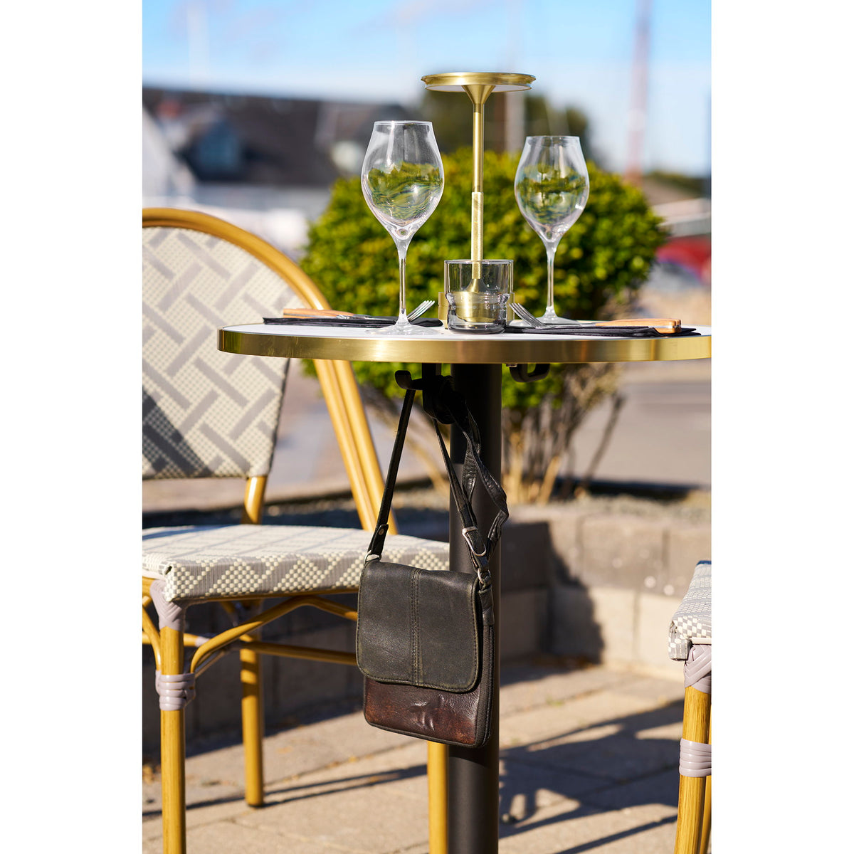 Table bistrot dressée de verres et d'une lampe dorée avec un sac suspendu à son crochet