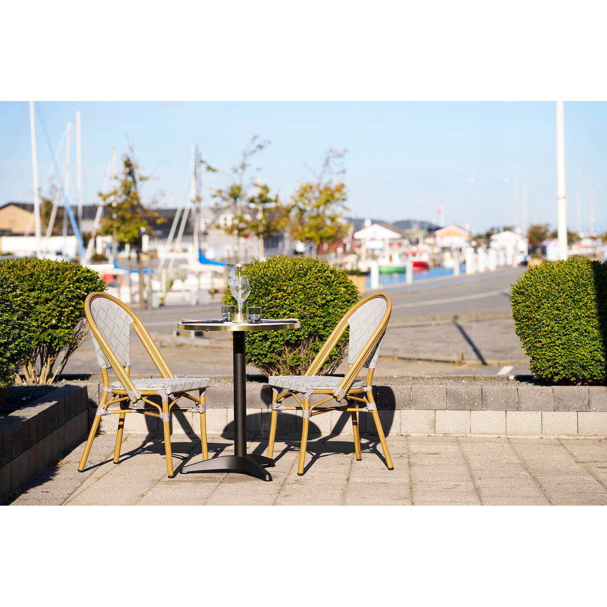Table bistrot ronde et deux chaises en terrasse face aux voiliers d'un port
