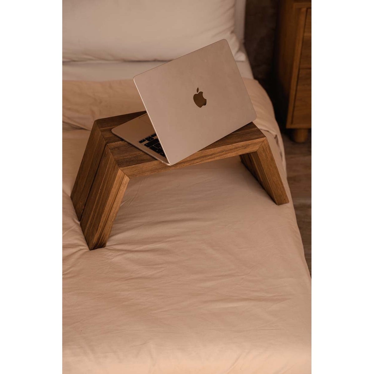 Table basse Ashley Cocoon en teck sur un lit aux draps clairs avec un ordinateur portable ouvert