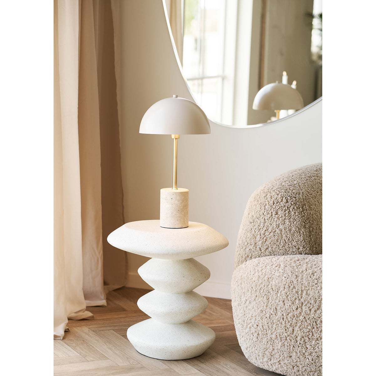 Table d'appoint Blackburn portant une lampe à pied de travertin à côté d'un fauteuil bouclé