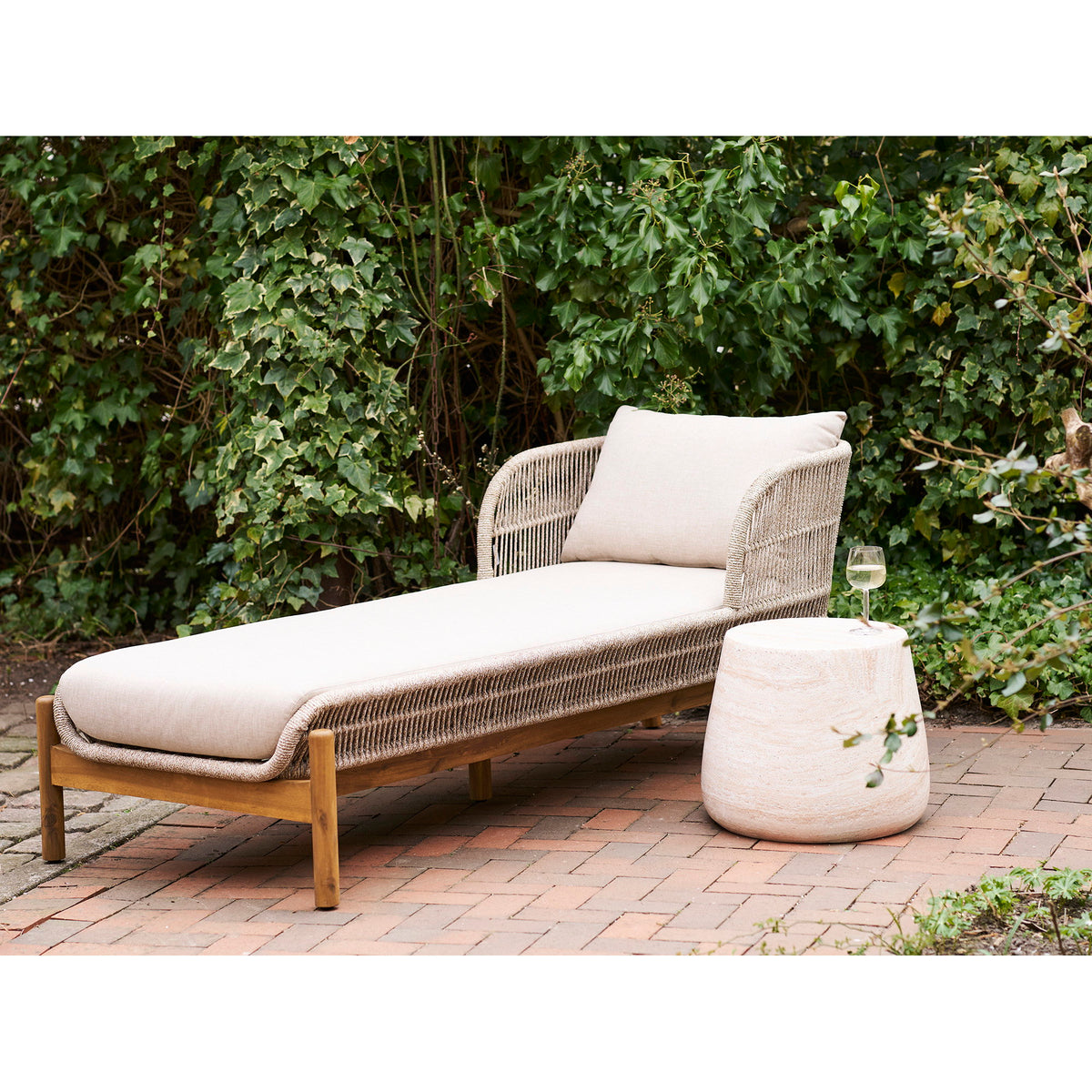 Table d'appoint Bonn effet travertin à côté d'une chaise longue en corde tressée et bois dans un jardin