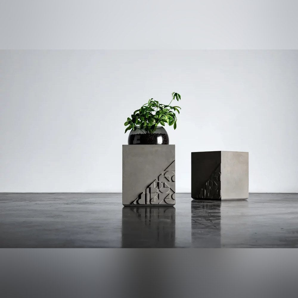 Deux tables d'appoint Curb en béton dont l'une porte une plante dans son globe en verre