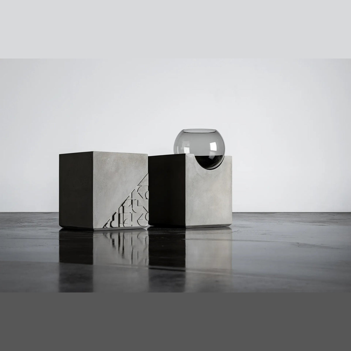 Deux tables d'appoint Curb en béton dans un studio l'une sans globe côté bas-relief l'autre avec son globe en verre fumé