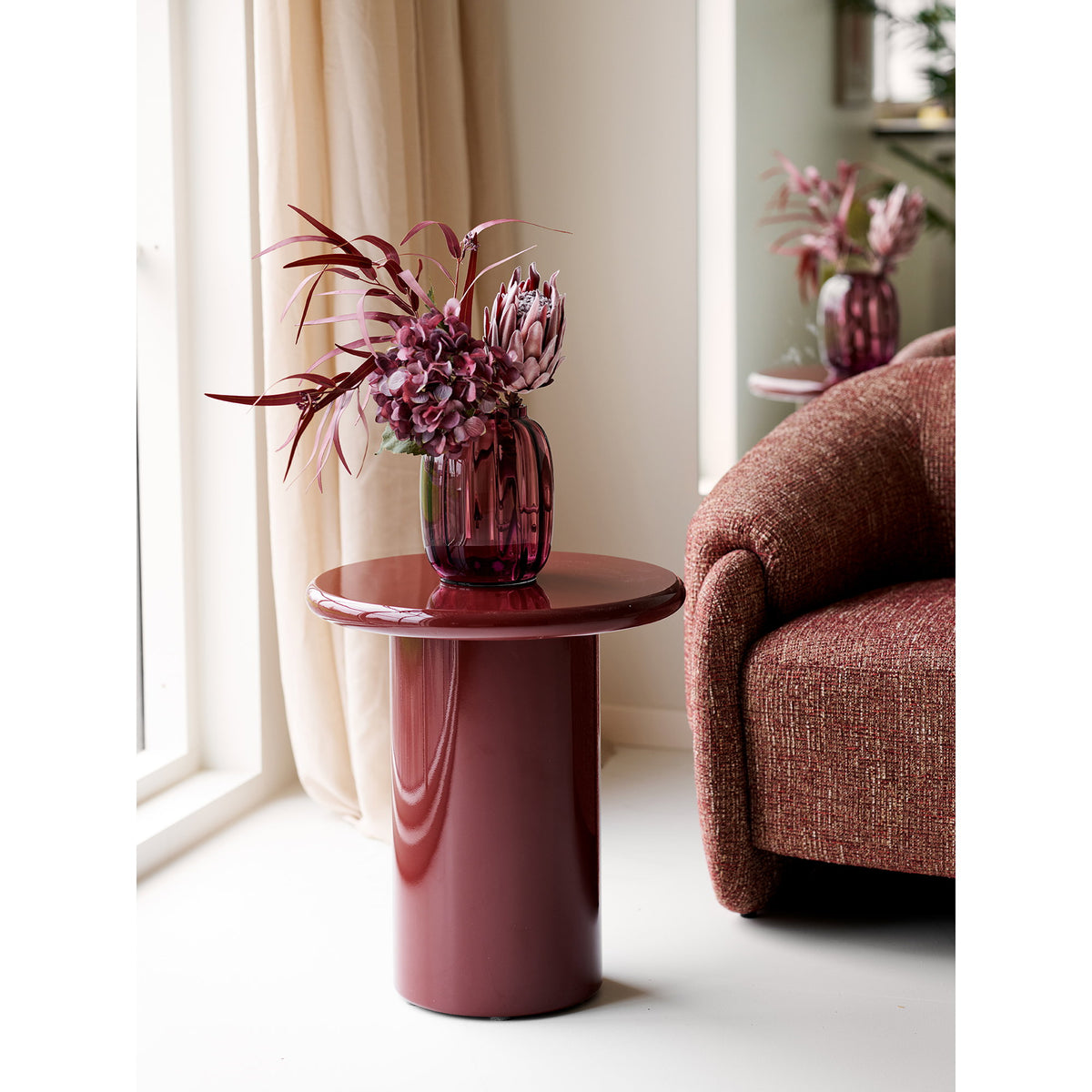 Table d'appoint Otago bordeaux avec un vase en verre côtelé et des fleurs prune devant un rideau clair