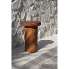 Table d'appoint Inti en bois posée au soleil devant un mur de pierre blanche