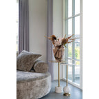 Table d'appoint Salo près d'une fenêtre à côté d'un canapé rond en tissu texturé et d'une table plus haute portant un bouquet dans un vase en verre