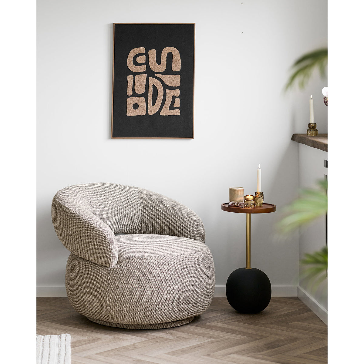 Table d'appoint Sirone portant une bougie et des photophores à côté d'un fauteuil en bouclé sous une toile graphique