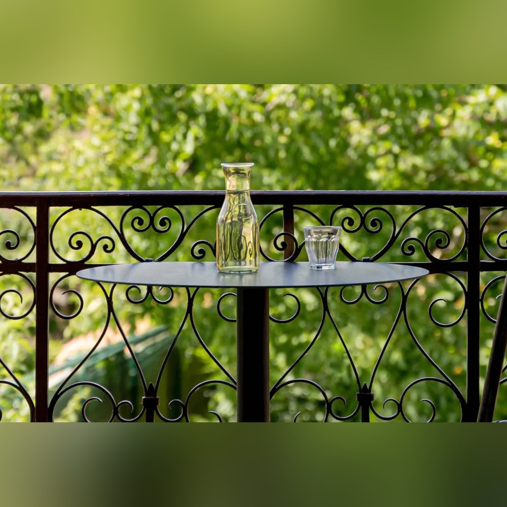 Plateau noir de la table de bistro Donut avec une carafe et un verre devant une rambarde en fer forgé