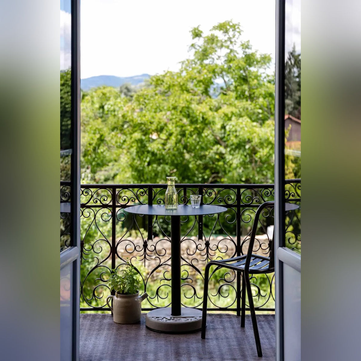 Table de bistro Donut avec une carafe et un verre sur un balcon contre une rambarde en fer forgé près d'une chaise noire