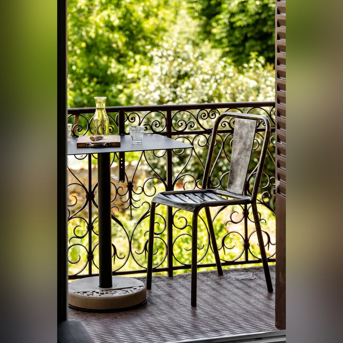 Table de bistro Donut rectangulaire sur un balcon en fer forgé avec une chaise en métal une carafe et deux verres