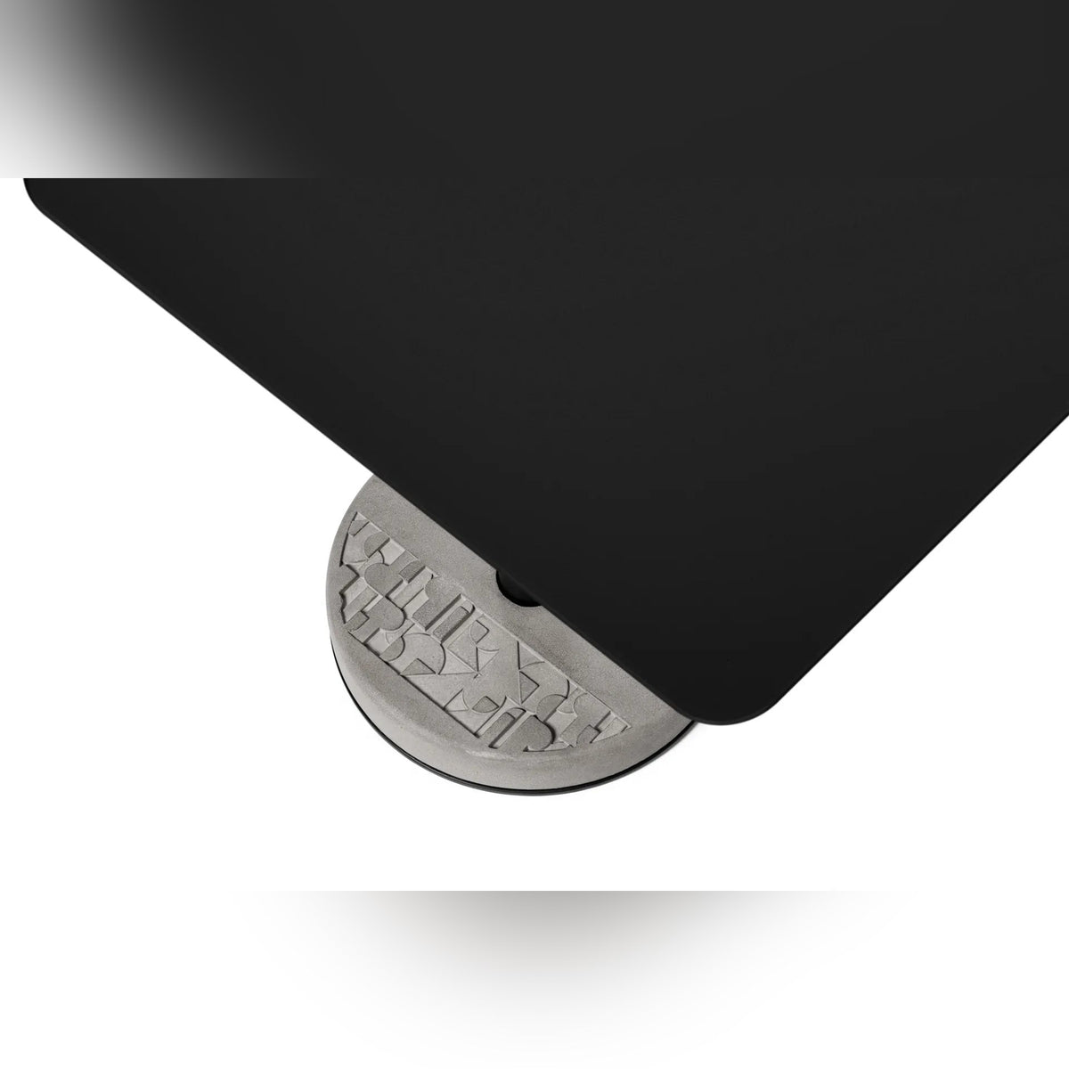 Vue plongeante sur l'angle du plateau en aluminium noir et le motif en relief du socle en béton de la table Donut