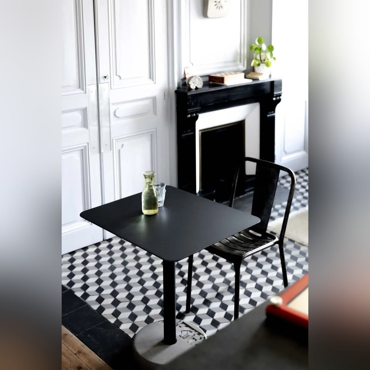 Table de bistro Donut rectangulaire sur des carreaux de ciment devant une cheminée noire avec une chaise en métal