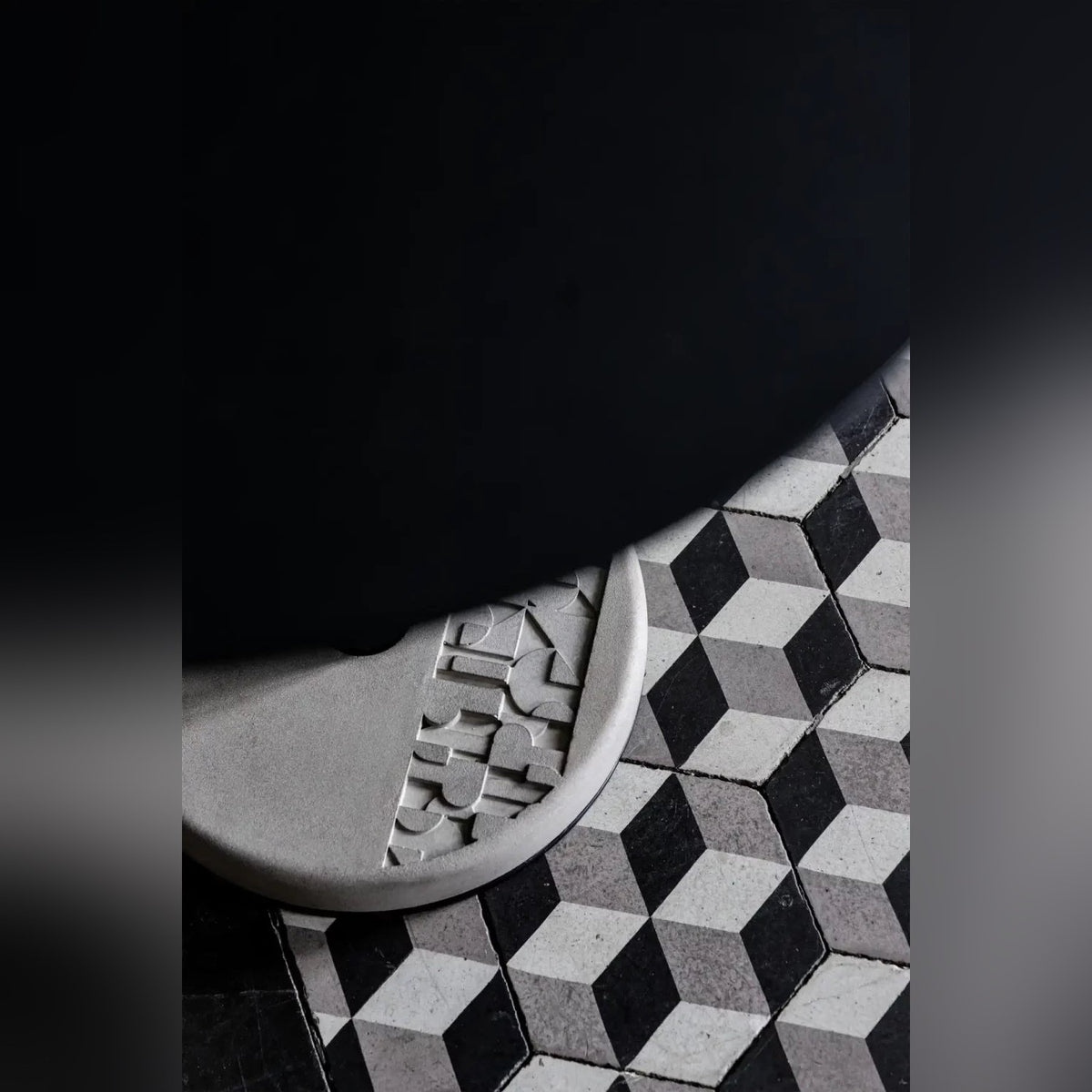 Socle en béton à motif en relief de la table Donut sur un sol de carreaux à cubes noirs et gris