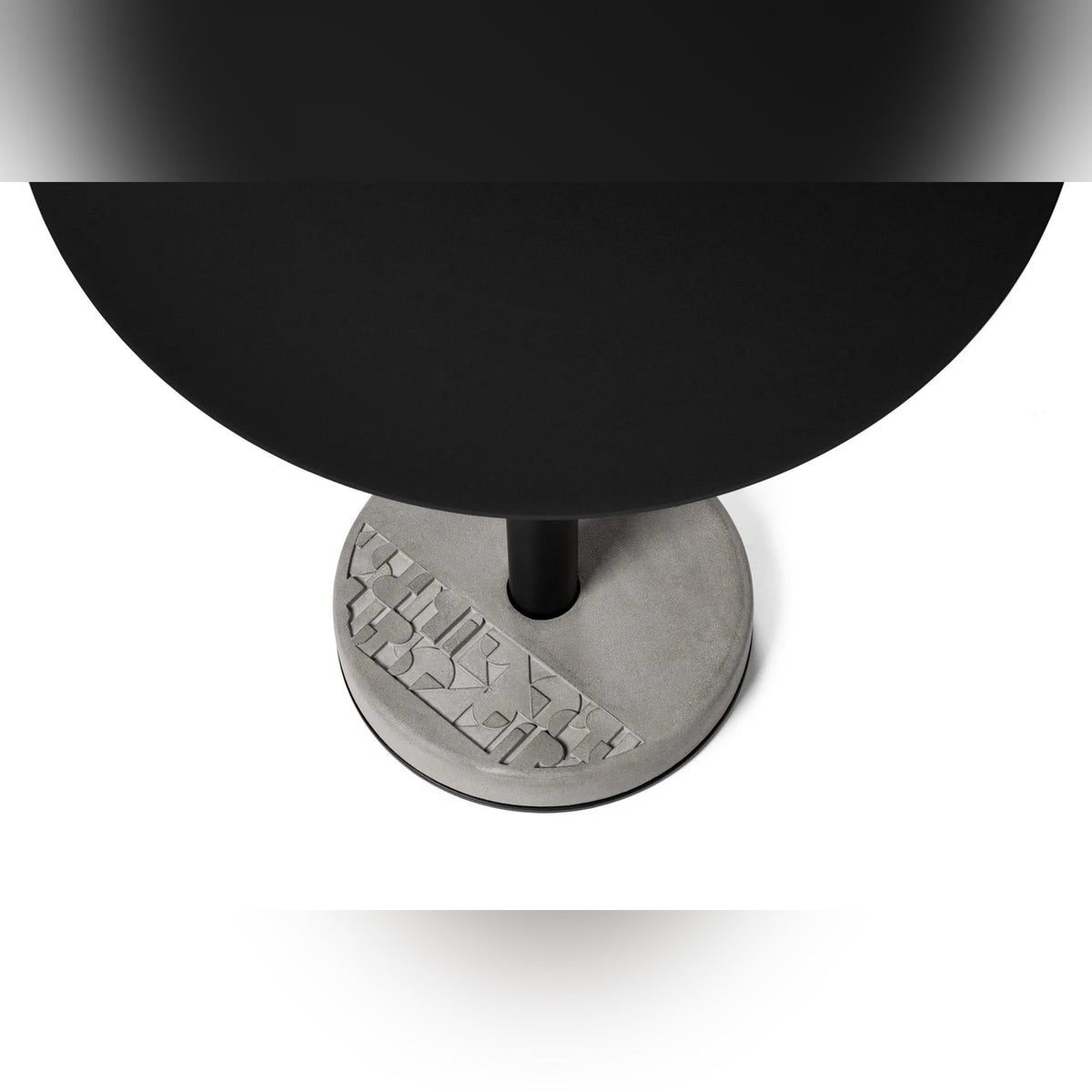 Vue plongeante sur le plateau rond noir et le socle en béton à motif géométrique de la table Donut