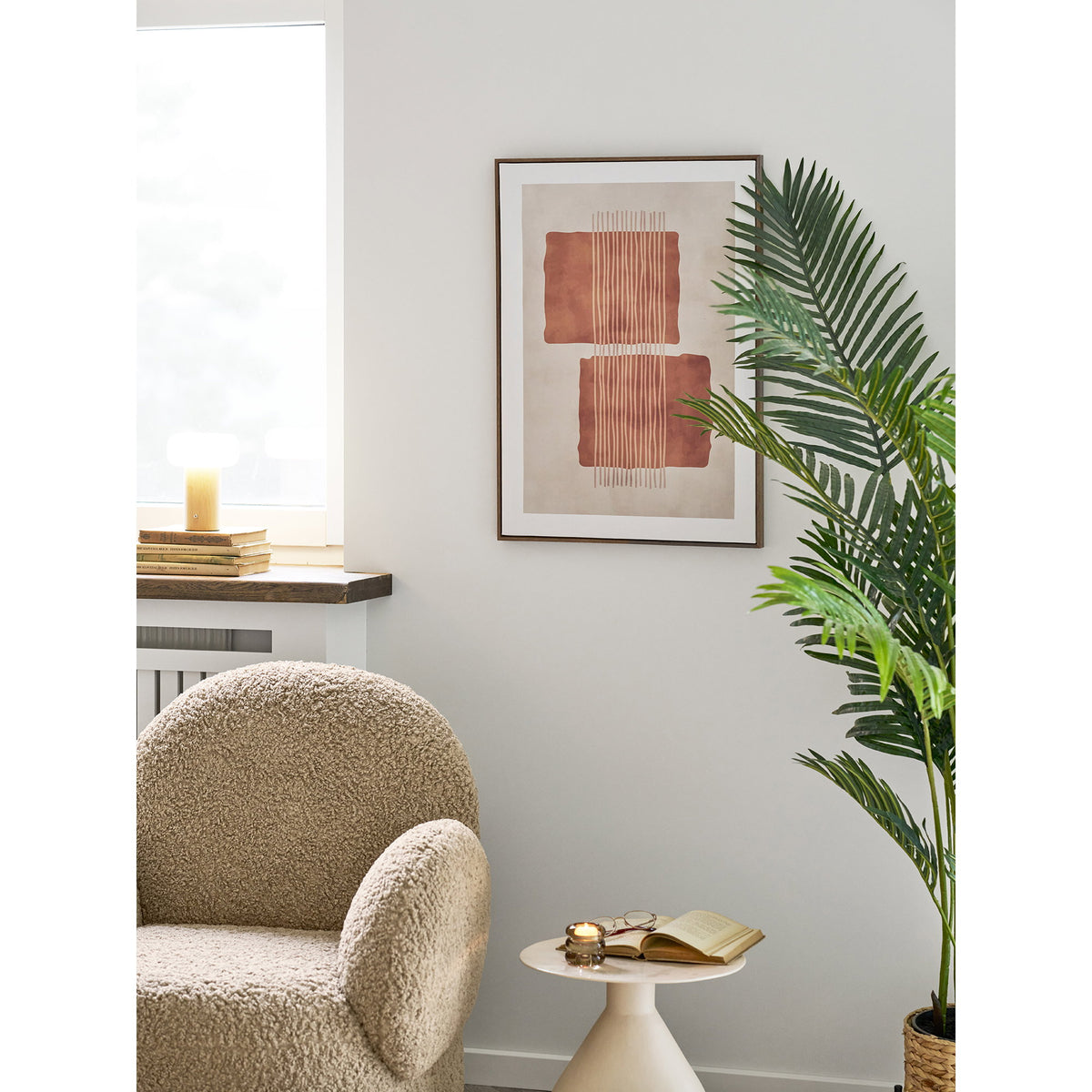 Tableau Mina N°2 accroché sur un mur clair au-dessus d'une table d'appoint près d'un fauteuil bouclé