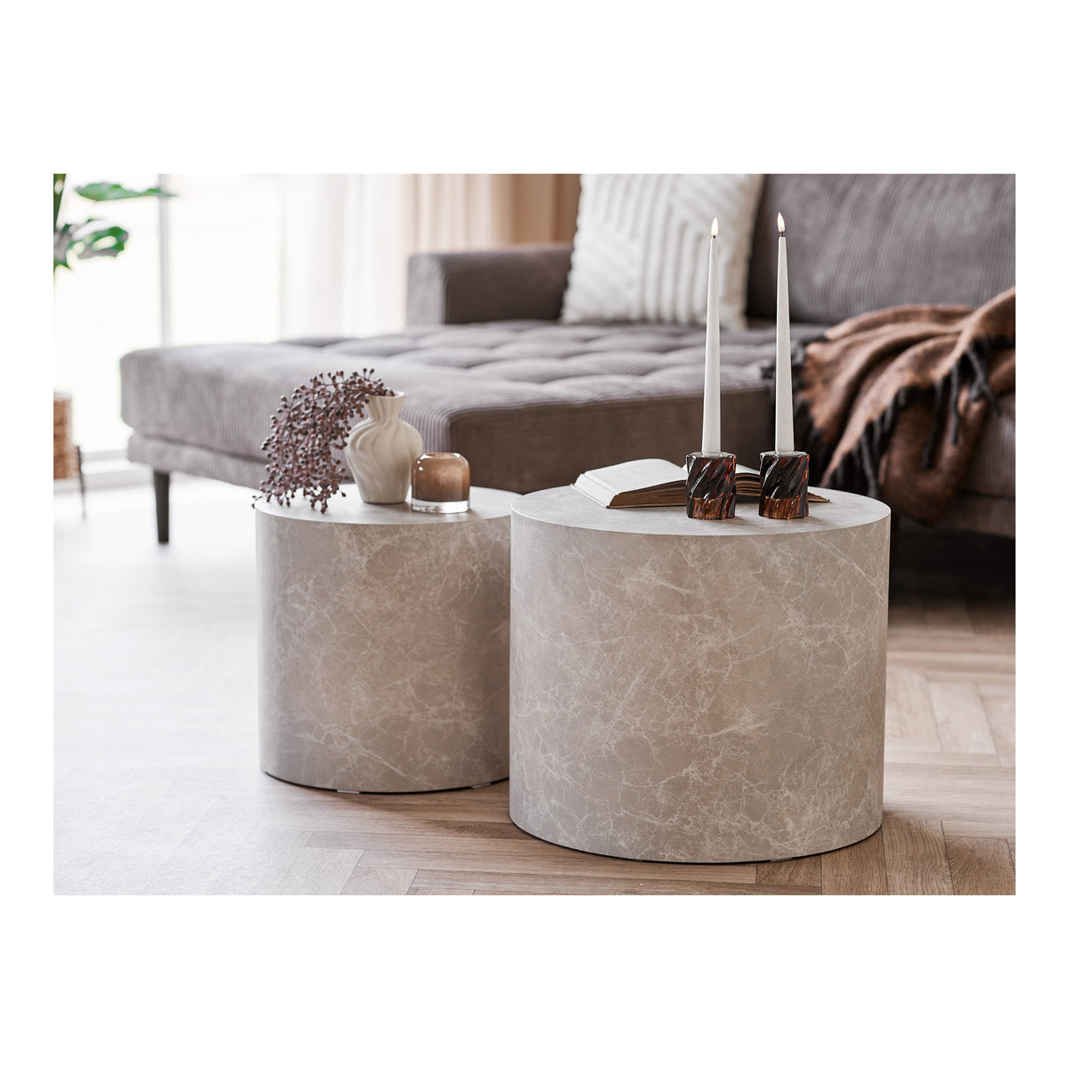 Tables basses rondes Prague effet marbre beige devant un canapé gris avec bougies livre et vase