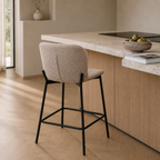 Tabouret de bar en tissu bouclé beige à piètement métal noir, installé de dos contre un îlot de cuisine en bois clair