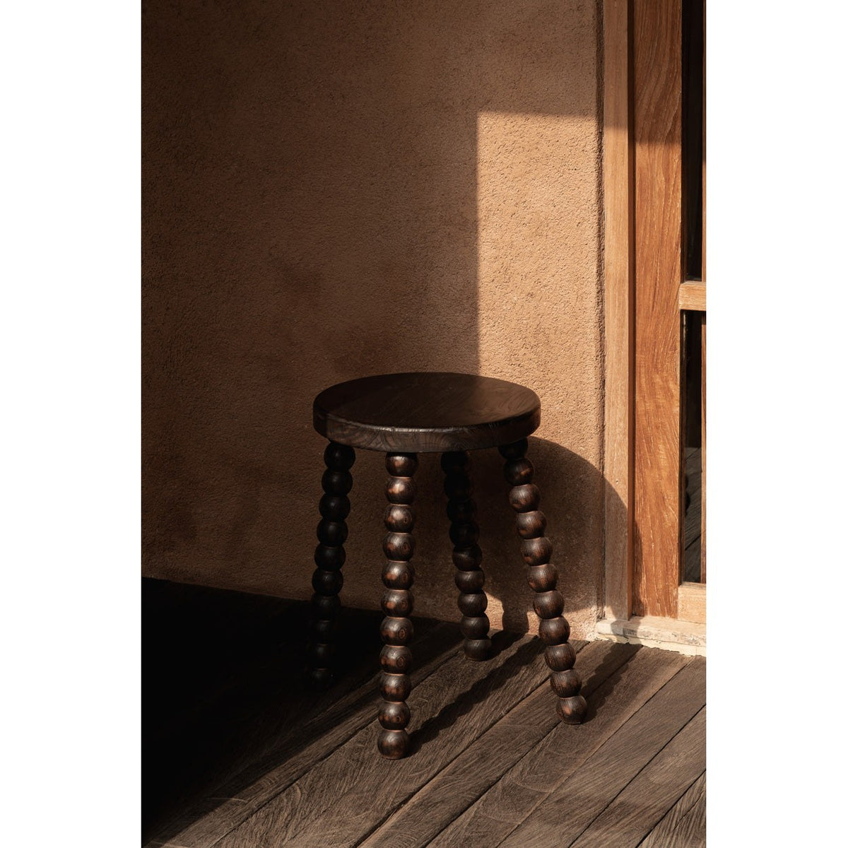 Tabouret Dango dans un rayon de soleil contre un mur enduit sur un plancher en bois