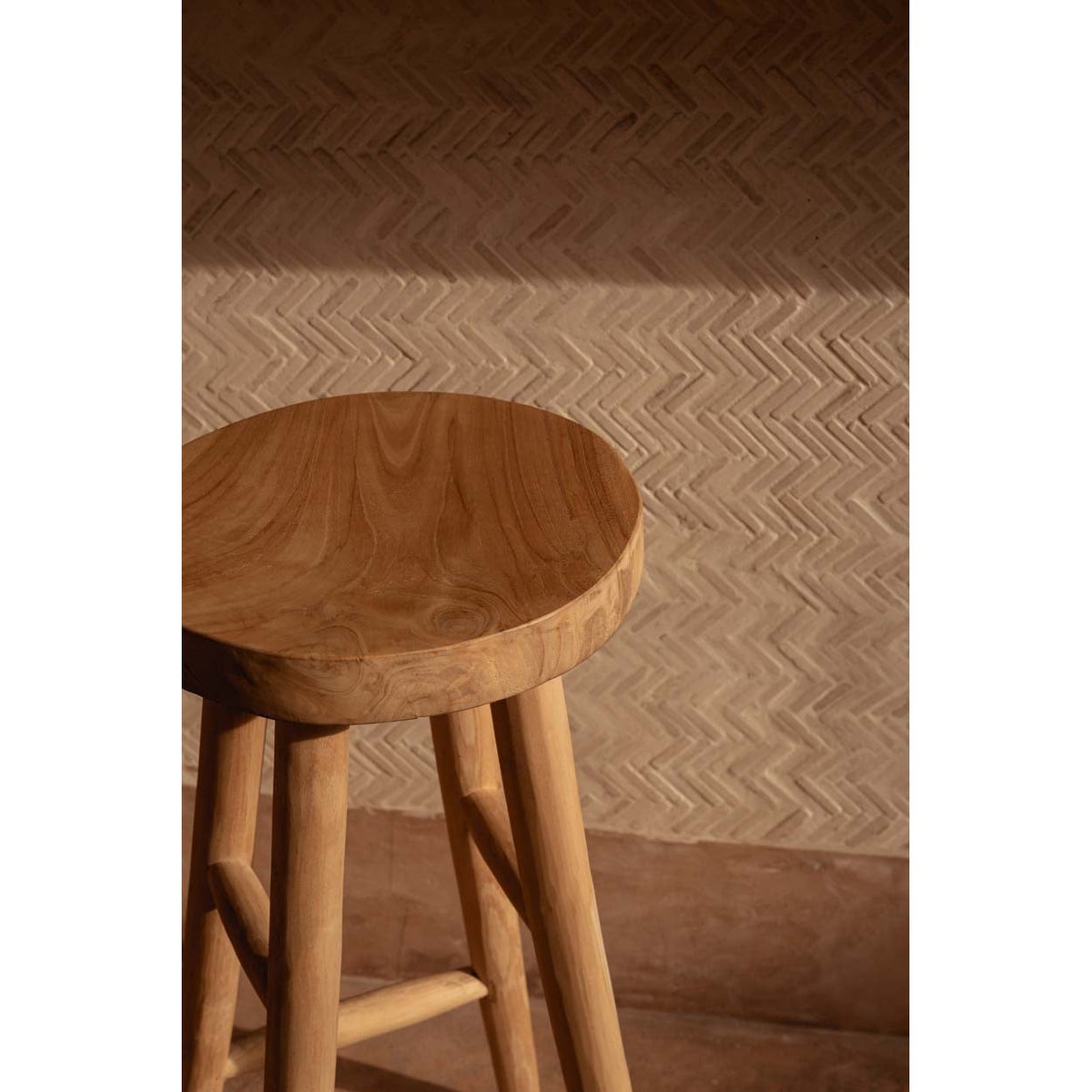 Détail de l'assise ronde en teck veiné du tabouret Kedut devant un mur à chevrons