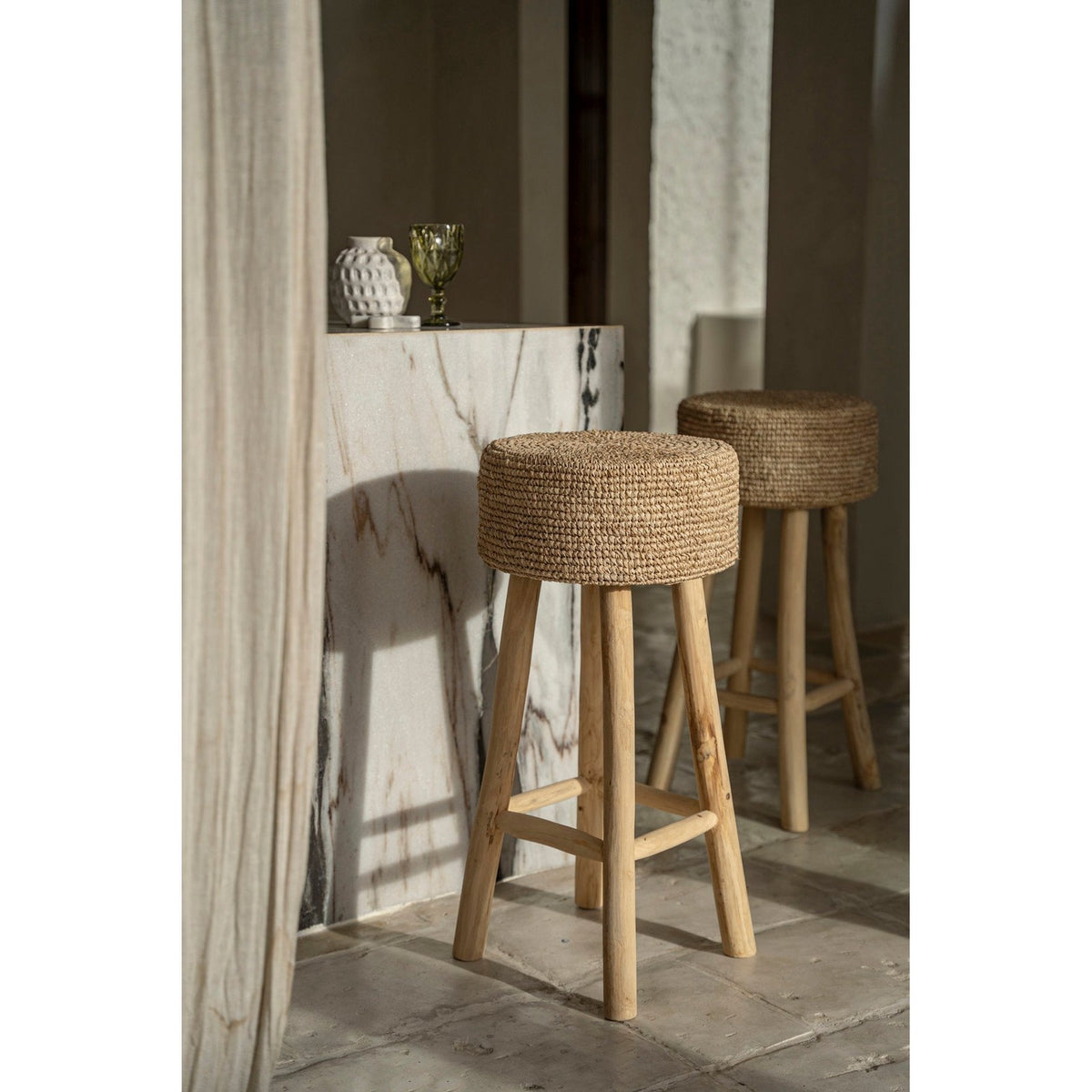 Tabourets de bar Raffia en teck et raphia au pied d'un bar en marbre baignés de soleil