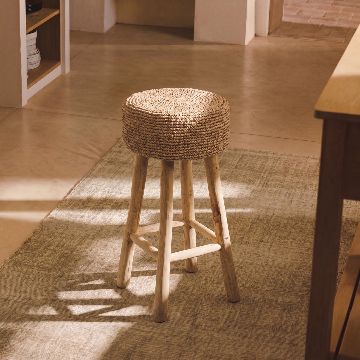 Tabouret de bar Raffia posé sur un tapis tissé dans une cuisine baignée de soleil