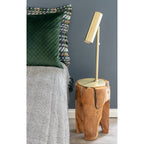 Tabouret Rose en teck en table de chevet avec une lampe dorée à côté d'un lit
