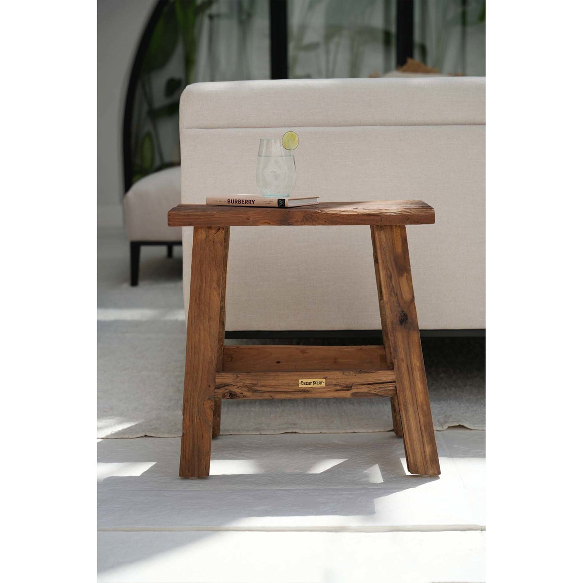 Tabouret rustique Fab en teck vu de face devant un canapé beige