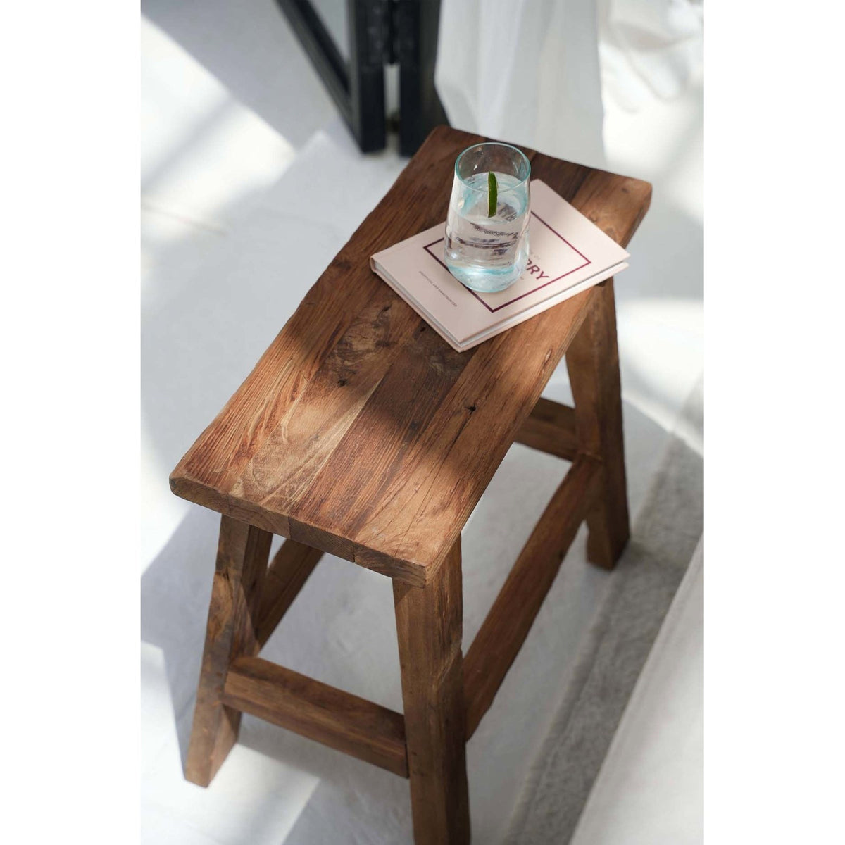 Vue plongeante sur l'assise en planches de teck du tabouret Fab avec un verre posé sur un livre