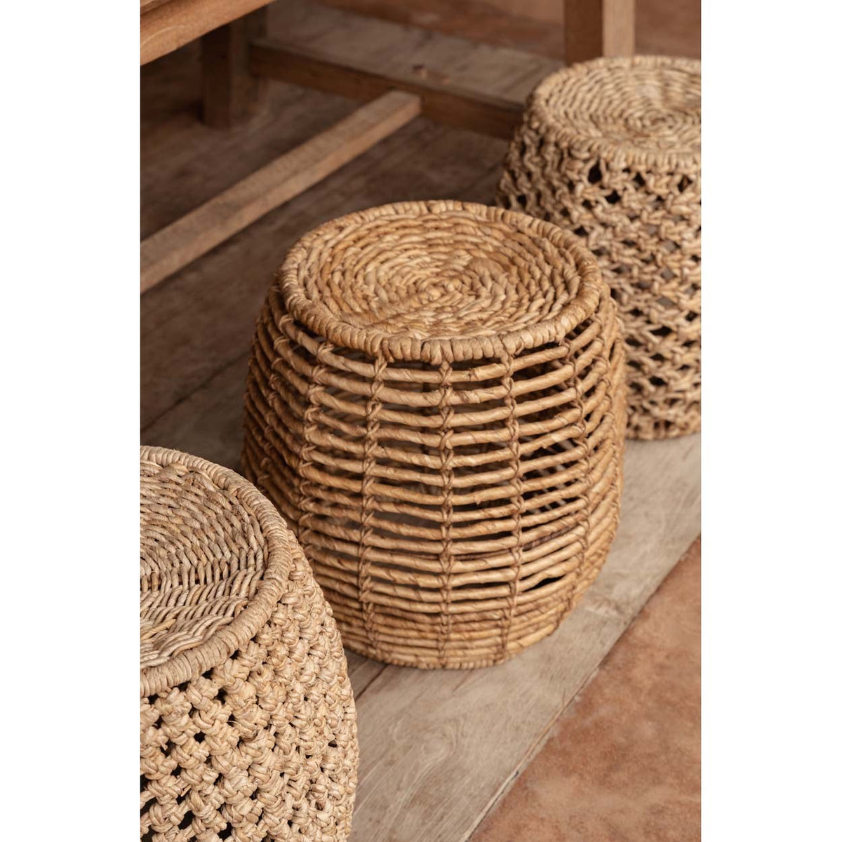 Tabouret Gustih au premier plan entre deux autres tabourets tressés sur un plancher en bois