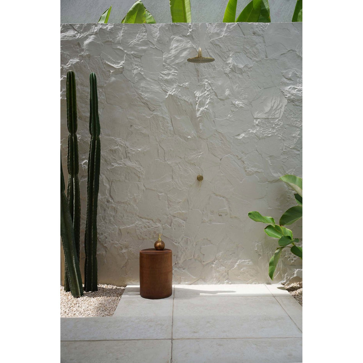 Tabouret Tribe bois clair au pied d'une douche extérieure près de grands cactus