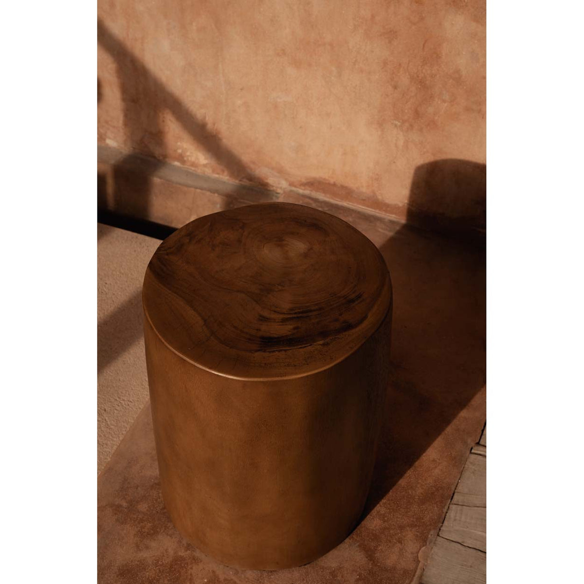 Tabouret Tribe bois clair vu de dessus devant un mur en terre ocre