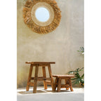 Tabourets Yoke petit et grand modèle en teck recyclé devant un mur enduit sous un miroir rond frangé