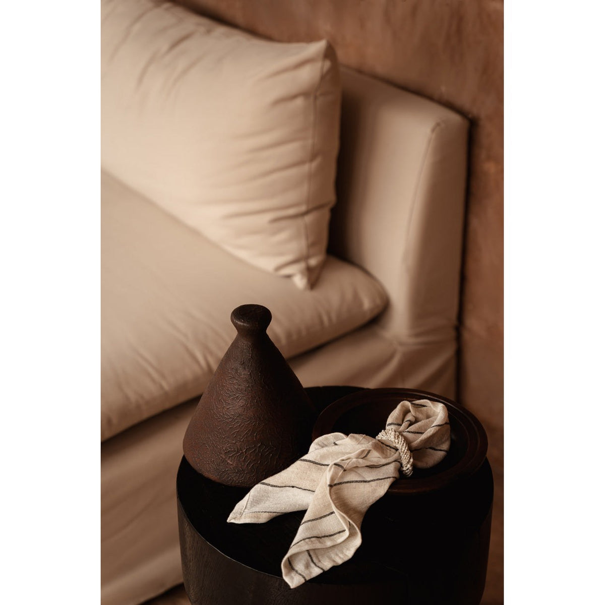 Tajine en terre cuite sur une table d'appoint en bois sombre près d'un canapé beige