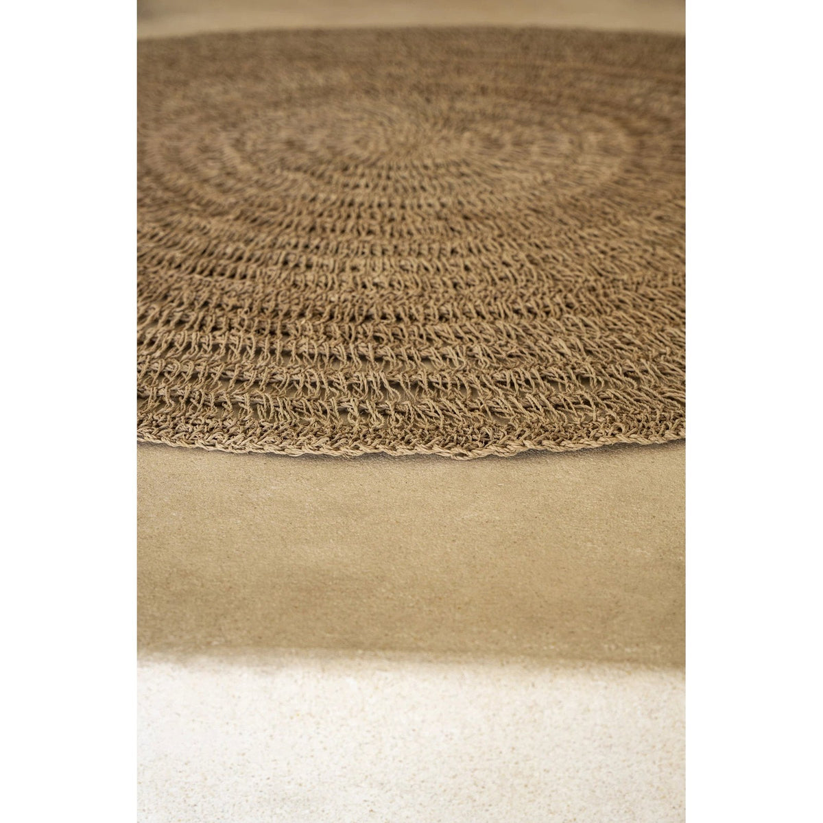 Détail de la bordure et des rangs ajourés d'un tapis rond en jonc de mer sur un sol beige