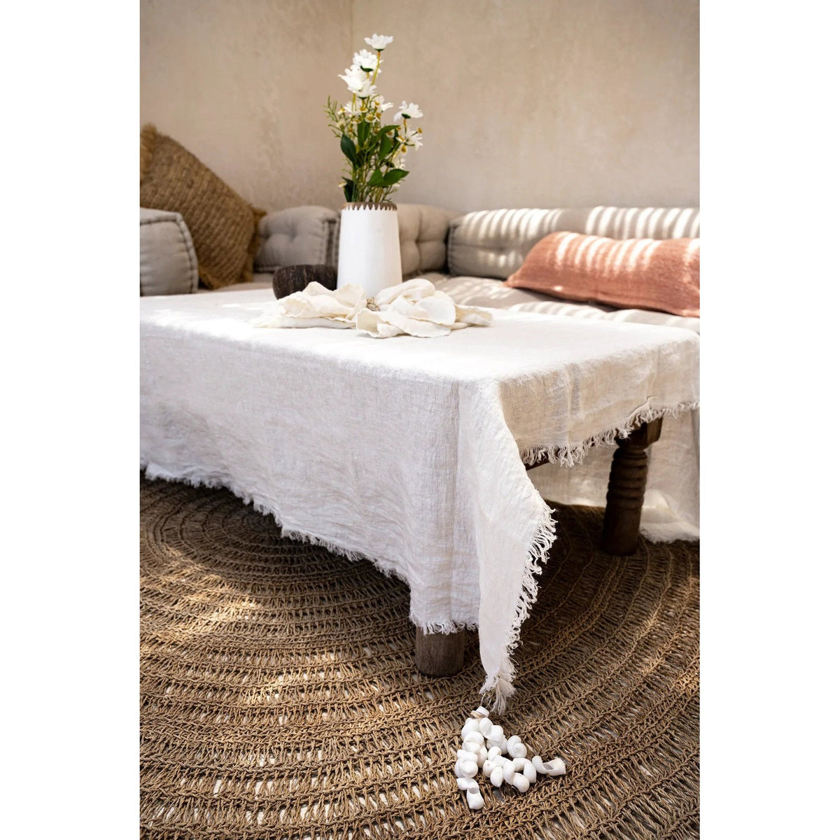 Tapis rond en jonc de mer sous une table basse couverte d'une nappe blanche à franges devant une banquette