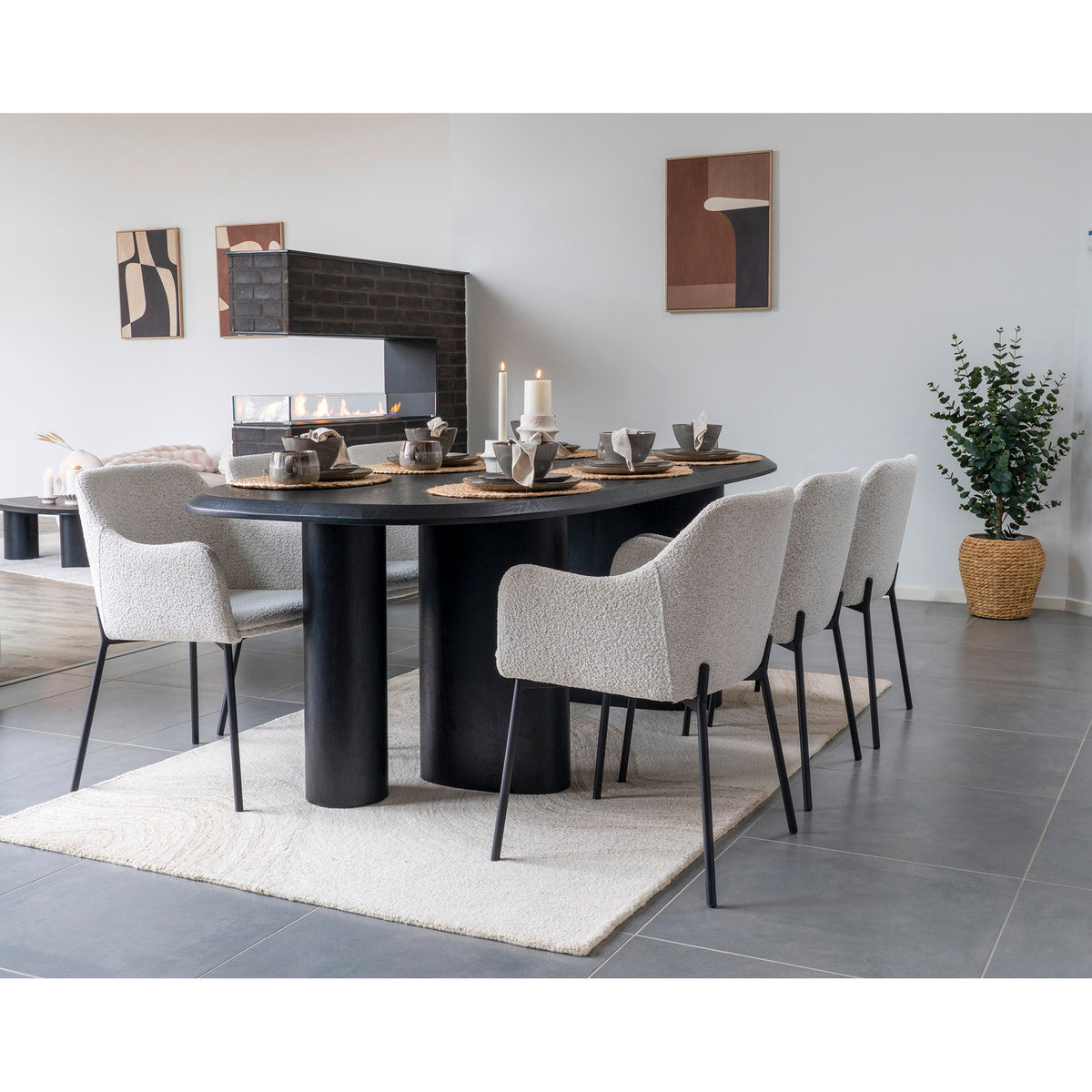 Tapis Surat sous une table ovale noire à pieds cylindriques entourée de fauteuils bouclés devant une cheminée